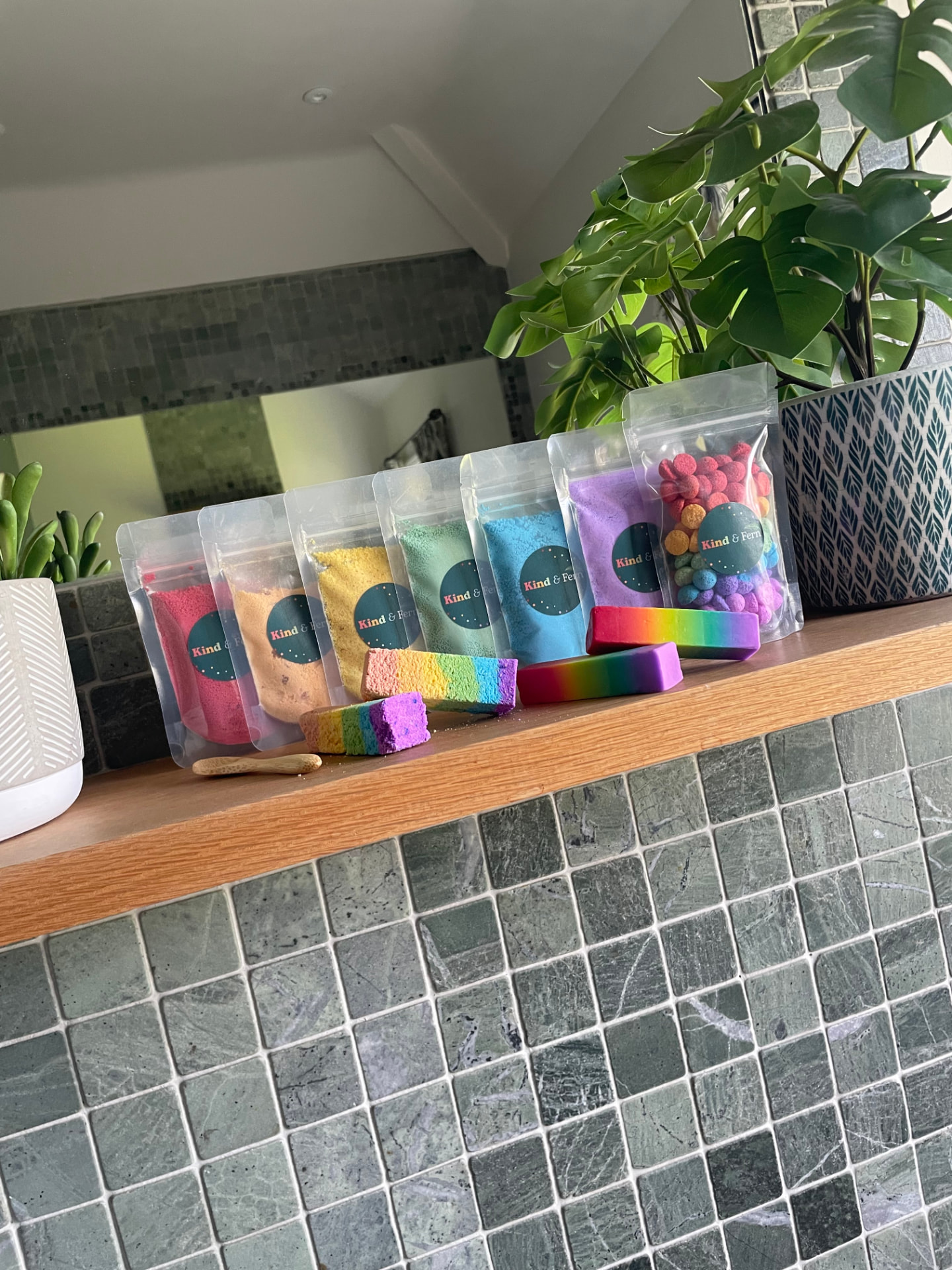 Close-up of Kind & Fern rainbow bath dust pouches, bath blocks and bath teenies on a wooden bathroom shelf