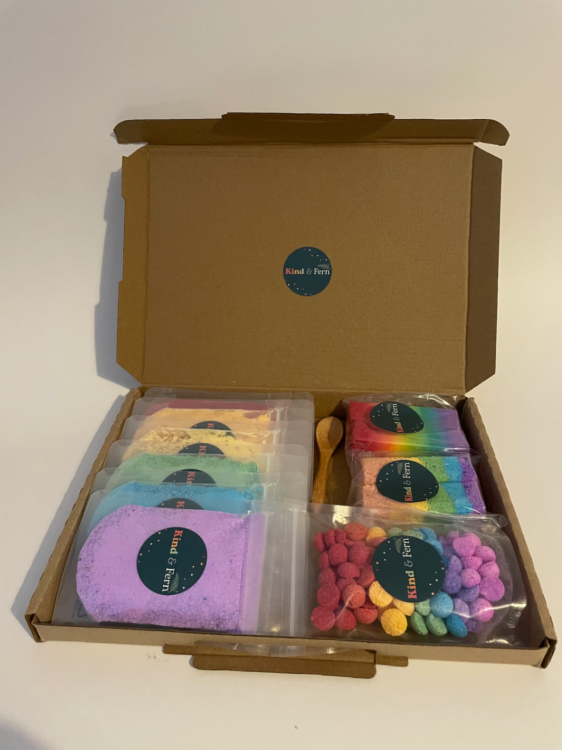 An open Kind & Fern Rainbow box filled with bath dust pouches, bath blocks, bath teenies and a wooden scoop